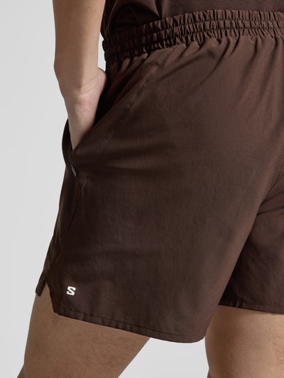 Mannenmodel draagt Shorts mit elastischem Bund und Eingrifftaschen van Salomon in regular fit, bruin, logo, detailopname heupen.