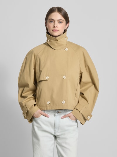 Vrouwenmodel draagt trenchcoat met mouwsluitingen model 'MIA' van Topshop in beige, puur katoen, regular fit, met dubbele rij knopen, platte kraag, knoopsluiting; ruglengte maat S 53 cm, schouderbreedte 52 cm, borstwijdte 54 cm, mouwlengte 64 cm; vooraanzicht bovenlichaam
