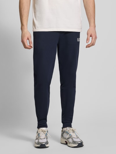 Männermodel trägt Sweatpants mit Logo und elastischem Bund von EA7 Emporio Armani in Dunkelblau, Regular Fit, Ganzkörperansicht von vorne.