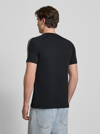 Männermodel trägt Regular Fit T-Shirt aus Baumwoll-Mix mit JFA-Applikation Modell 'NOIR' von adidas Originals in Optik: Unifarben, Schwarz, Logo-Stitching, Kontraststreifen, Rundhals, Kurzarm, Material: Baumwoll-Mix, Ganzkörperansicht Rückansicht.