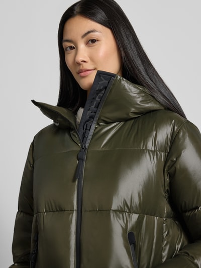 Frauenmodel trägt Mantel mit Kapuze Modell 'SELECTRIC' von Peuterey, olivgrün glänzend, sichtbare Steppnähte, Nahaufnahme Oberkörper.