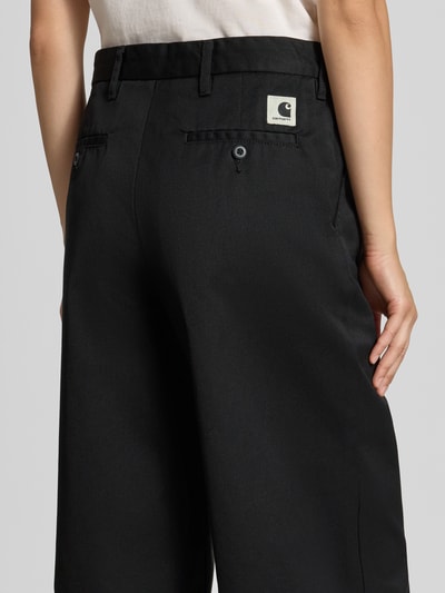 Vrouwenmodel draagt Straight Fit broek met ritssluiting Model 'Omak' van Carhartt Work In Progress in katoenmix met steekzakken achter, Ganzkörperansicht Rückansicht.