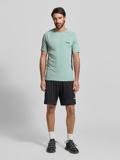 Męski model nosi Slim Fit T-Shirt mit Label Print Modell 'TOP SPIN CB' od BOSS Green, jednolity kolor, krój slim fit, nadruk z logo, okrągły dekolt, krótki rękaw, widok całej sylwetki z przodu.