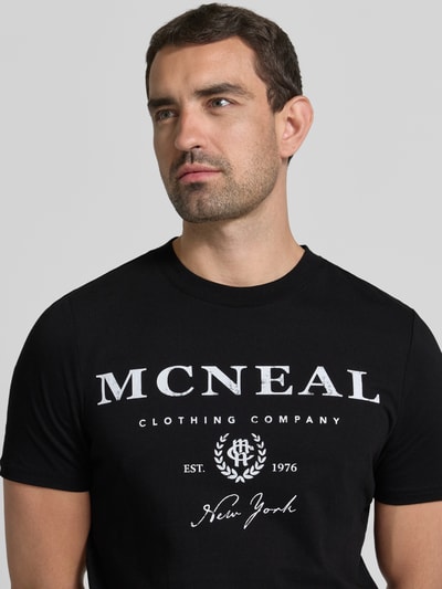 Männermodel trägt T-Shirt mit Label-Print und Rundhalsausschnitt von MCNEAL, czarny, bawełna, krój regular fit, długość tyłu 68 cm w rozmiarze M, nadruk z logo z przodu, okrągły dekolt, męski t-shirt, zbliżenie na górną część ciała