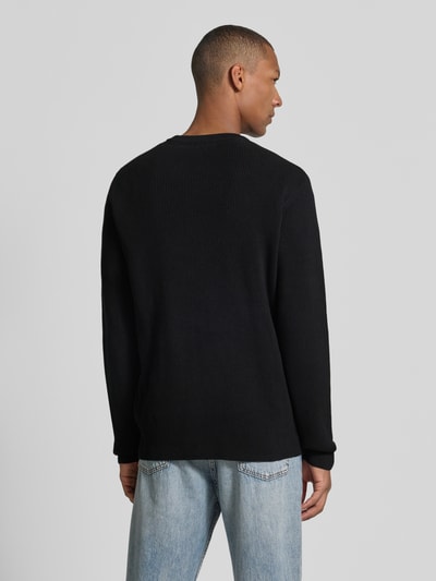 Männermodel trägt Slim Fit Strickpullover Baumwoll-Mix von Lindbergh, gerippte Optik, schwarze Farbe, Ganzkörperansicht Rückansicht.