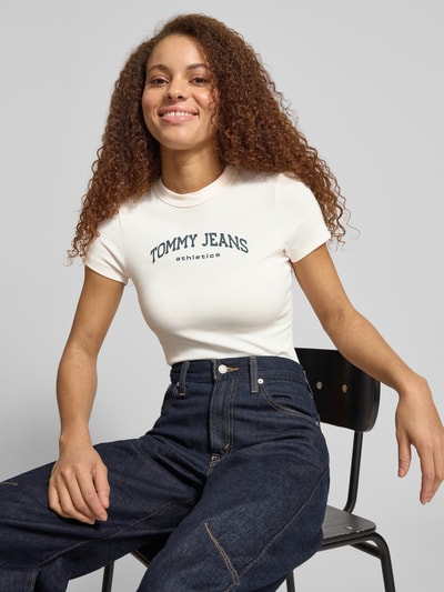 Vrouwenmodel draagt Slim Fit T-shirt uit katoenmix Model 'SLIM VARSITY' van Tommy Jeans, look: effen, pasvorm: slim fit, labelprint, ronde hals, korte mouw, katoenmix. Nahaufnahme Oberkörper.