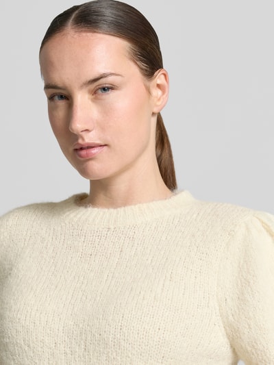 Kobieta nosi sweter z dodatkiem wełny Regular Fit model 'NOVAH' od VERO MODA w kolorze kremowym, widoczne faktura dzianiny, zbliżenie na górę ciała.