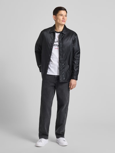 Męski model nosi Kurtkę Oversized Jacke mit Umlegekragen Model 'EVINUZ' od HUGO, jednokolorowy efekt, krój oversized, wykładany kołnierz, zapięcie na guziki, wyhaftowane logo, długi rękaw z mankietami, wpuszczane kieszenie, widok całej sylwetki z przodu.