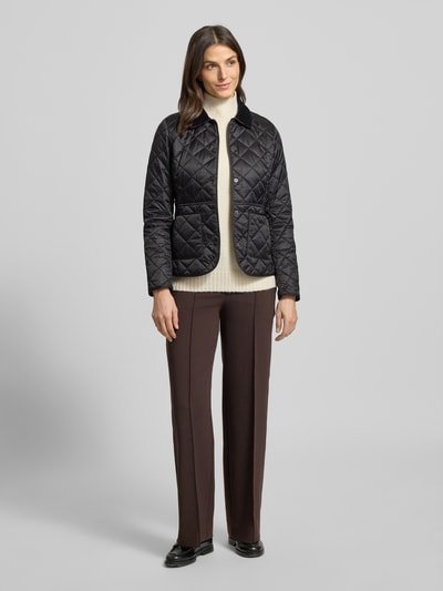 Kobiece model prezentuje kurtkę pikowaną z sztruksowym kołnierzem Model 'Deveron' od Barbour, czarny, taliowany krój, nakładane kieszenie, watowanie, logo Barbour na piersi, listwa z zatrzaskami, pikowanie; długość tyłu 60 cm, szerokość ramion 38 cm, długość rękawów 63 cm; widok na całe ciało z przodu.