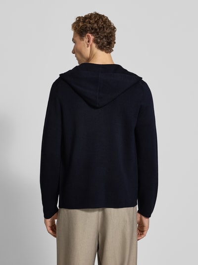 Männermodel trägt Regular Fit Strickjacke mit Lanawoll-Anteil von Christian Berg Men, dunkle Farbe, glatte Textur, Ganzkörperansicht Rückansicht. Material-Mix, Kapuze, langärmliges Design, Rückenlänge bei Größe M 67 cm, Ärmellänge 70 cm.