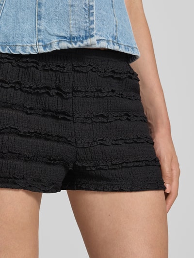 Frauenmodel trägt Shorts mit elastischem Bund Modell 'VILMA' von NOISY MAY®, schwarzes Strukturmuster, körpernaher Sitz, Nahaufnahme Oberschenkel.