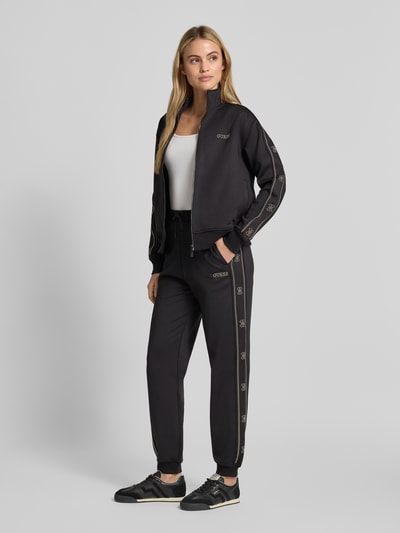 Vrouwenmodel draagt Relaxed Fit Sweatjacke aus elastischem Viskose-Mix van GUESS, zwart met sierrand, Strass-steentjes, labeldetail, activewear, Ganzkörperansicht van voren.