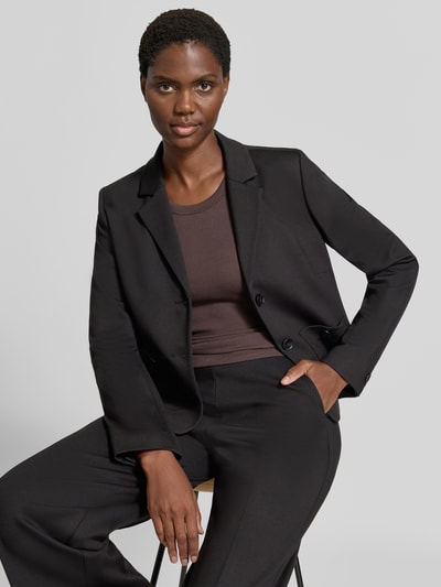 Frauenmodel trägt Blazer aus Viskose-Mix mit Reverskragen von MORE & MORE, taillierte Passform, Schwarz mit zwei aufgesetzten Taschen, Nahaufnahme Oberkörper.