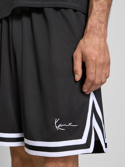 Männermodel trägt Relaxed Fit Shorts mit Logo-Stitching von KARL KANI aus schwarzem Mesh, elastischer Bund, Nahaufnahme Oberschenkel.