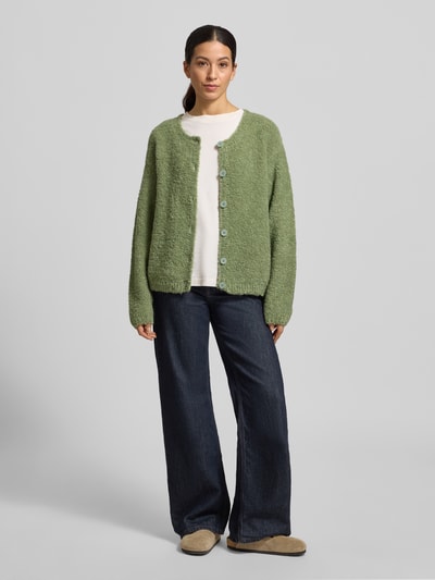 Frauenmodel trägt Strickjacke mit Knopfleiste Modell 'ZOLLY' von American Vintage in Hellgrün, lockerer Schnitt, Lanawoll- und Alpaka-Mix, Ganzkörperansicht von vorne.