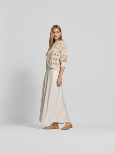Frauenmodel trägt Relaxed Fit Pullover mit Lochmuster von Juvia in Beige aus reiner Baumwolle, kombiniert mit cremefarbenem Rock, Ganzkörperansicht von vorne.