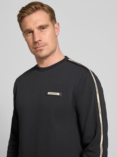 Männermodel trägt Sweatshirt mit Label-Details und Rundhalsausschnitt von EA7 Emporio Armani in Schwarz, Baumwoll-Mix, Regular-Fit, Nahaufnahme Oberkörper. Rückenlänge bei Größe M 63 cm, Ärmellänge 66 cm.