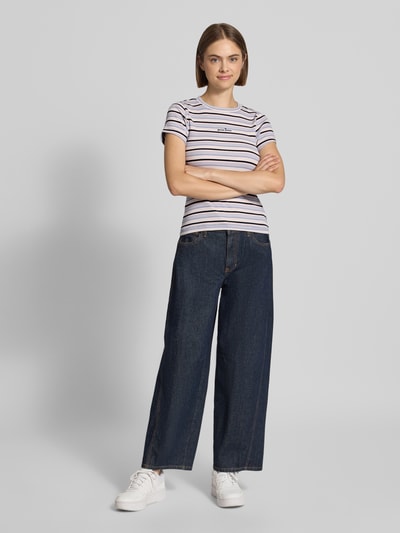 Frauenmodel trägt Slim Fit T-Shirt mit Logo-Stitching von GUESS, feine Streifen, elastischer Baumwoll-Mix, Ganzkörperansicht von vorne.