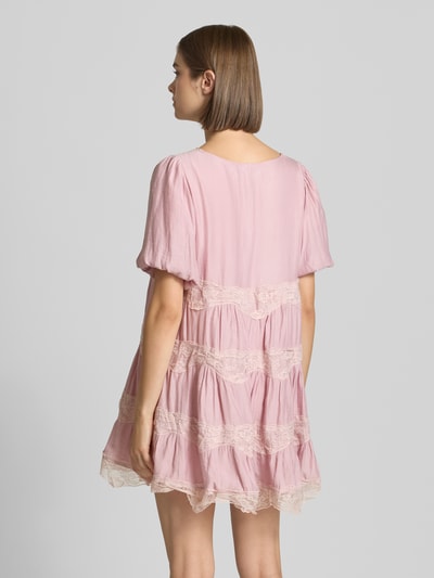 Männermodel trägt sukienka mini z obszyciem koronką, krój regular fit, model 'Cotton Candy' od DAISY STREET, jasnoróżowy z kremowymi detalami, krótki rękaw, dekolt w serek, długość tyłu w rozmiarze S: 78 cm, szerokość w rozmiarze S: 48 cm, długość rękawów w rozmiarze S: 26 cm, całość z lekkimi marszczeniami i delikatną fakturą materiału, widok całej sylwetki z tyłu.