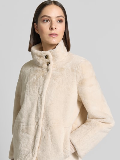 Modelka kobieca ma na sobie kurtkę 'Jacke aus Kunstfell mit Eingrifftaschen' od COMMA, beżowe sztuczne futro, krój regular fit, stójka, zapięcie na guzik, wpuszczane kieszenie, długość tyłu w rozmiarze 36: 54 cm, szerokość ramion w rozmiarze 36: 40 cm, szerokość klatki piersiowej w rozmiarze 36: 56 cm, długość rękawów w rozmiarze 36: 66 cm, faktura miękka, widoczne proste kształty, subtelny połysk, zbliżenie górnej części torsu z przodu.