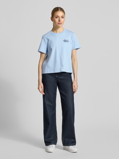 Kobiece modelka nosi damski t-shirt Regular Fit T-Shirt aus reiner Baumwolle Modell 'SARA' od Vero Moda, jednokolorowy, wyhaftowane logo, okrągły dekolt, krótki rękaw, dżersej, czysta bawełna, całkowity widok z przodu.