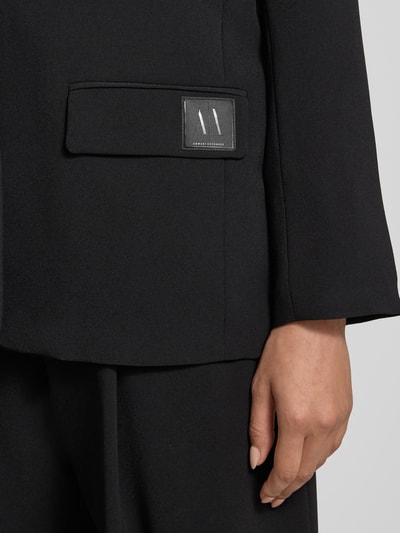 Frauenmodel trägt Relaxed Fit Blazer mit Reverskragen von ARMANI EXCHANGE in Schwarz mit Pattentasche und Knopfverschluss, Detailaufnahme.