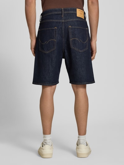 Männermodel trägt Relaxed Fit Jeansshorts Modell 'TONY' von Jack & Jones aus dunkelblauem Baumwoll-Elasthan-Mix mit Eingrifftaschen, Bundweite 42 cm, Innenbeinlänge 21 cm, Ganzkörperansicht Rückansicht.