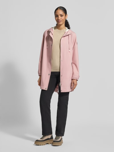 Frauenmodel trägt Jacke mit Ärmelriegeln von NAUTGÅRD in Rosa, kombiniert mit schwarzer Hose und beigen Schuhen, glatte Oberfläche, Ganzkörperansicht von vorne. Regular Fit, Kapuze mit Tunnelzug, Knopfleiste, Reißverschlusstaschen, Maße Größe S: Rückenlänge 90 cm, Schulterbreite 45 cm, Brustweite 51 cm, Ärmellänge 62 cm.
