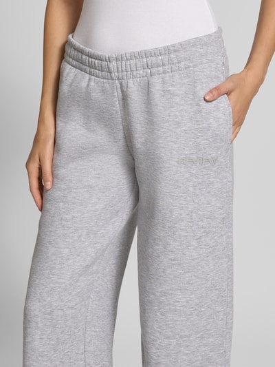Frauenmodel trägt Sweathose in grau melange mit geradem Bein von REVIEW, Baumwoll-Mix, elastischer Bund, Logo-Print, Nahaufnahme Oberkörper.