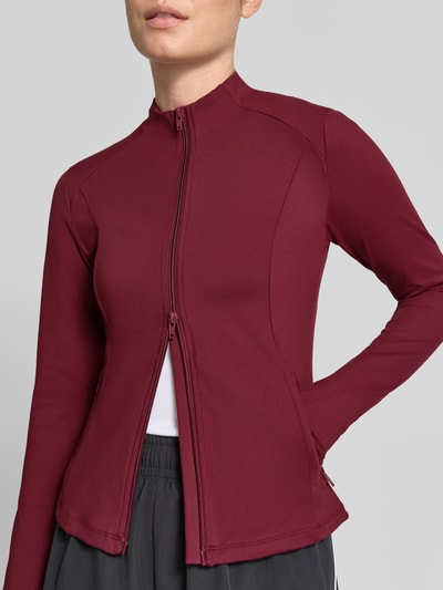Frauenmodel trägt Slim Fit Jacke mit Zweiwege-Reißverschluss Modell 'Sense' von aim'n in Dunkelrot, glatte Struktur, Nahaufnahme Oberkörper. Rückenlänge 28 cm, Schulterbreite 36 cm, Brustweite 35 cm.