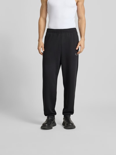 Männermodel trägt schwarze Sweatpants mit Label-Detail von Diesel aus reiner Baumwolle, lockerer Schnitt, elastischer Bund, Gesäßtasche, Ganzkörperansicht von vorne.