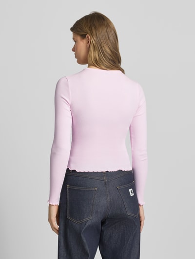 Kobiece modelka nosi Slim Fit Langarmshirt aus Baumwoll-Mix von Tommy Jeans w jasnoróżowym kolorze, drobne prążkowanie, długi rękaw, detal z logo, wykończenie z falbaną, mieszanka bawełny, widok całej sylwetki z tyłu.