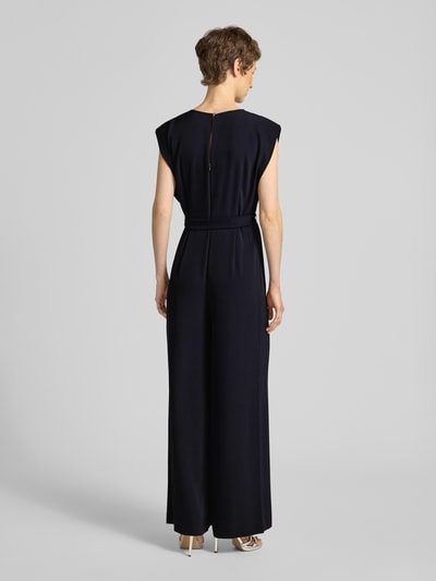 Frauenmodel trägt Jumpsuit mit V-Ausschnitt und Bindegürtel von comma in Dunkelblau, Material-Mix mit Stretch, Ganzkörperansicht Rückansicht.
