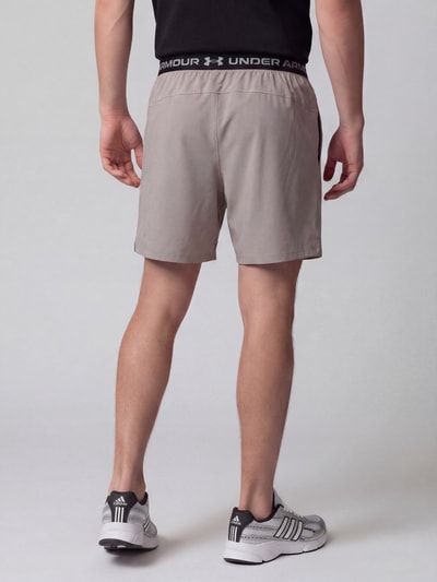 Männermodel trägt Regular Fit Sportshorts mit Logo-Print von Under Armour in Hellgrau mit schwarzem Bund, Herren Sportshorts, Ganzkörperansicht Rückansicht.