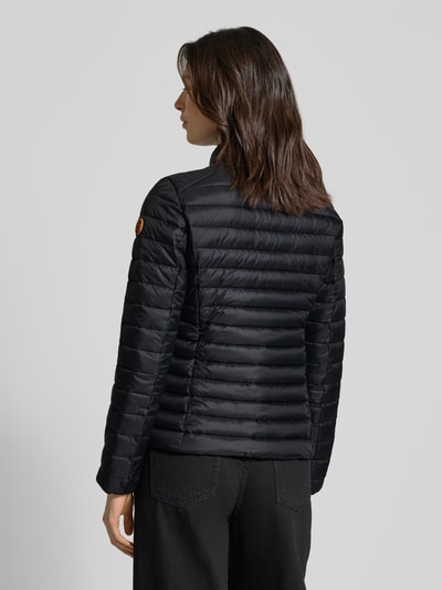 Modelka nosi czarną Kurtkę pikowaną o kroju slim fit z ocieplaną stójką, model 'Carly' od SAVE THE DUCK, z efektem pikowania, zamek błyskawiczny dwustronny, wpuszczane kieszenie zapinane na zamek błyskawiczny, długość tyłu w rozmiarze S: 58 cm, szerokość ramion w rozmiarze S: 40 cm, szerokość klatki piersiowej w rozmiarze S: 48 cm, długość rękawów w rozmiarze S: 62 cm, widok całej sylwetki z tyłu.