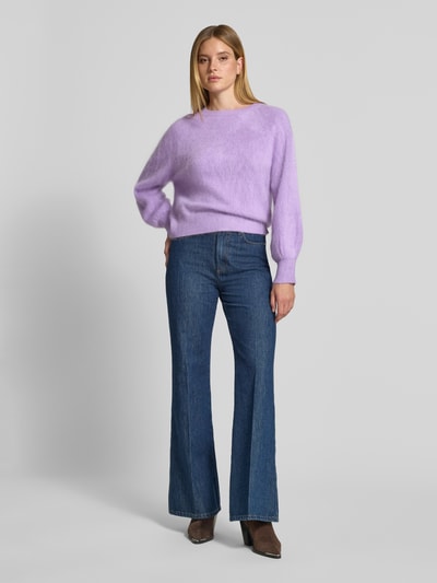 Frauenmodel trägt Regular Fit Pullover aus Kaschmir-Mix mit Woll-Anteil von HERZENS in Flieder, Strick-Optik, elastische Ärmel, Ganzkörperansicht von vorne.