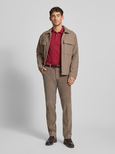 Mężczyzna-model nosi Poloshirt mit Label-Stitching od Christian Berg Men, kolor bordowy, krój slim fit, bawełna, z polokołnierzykiem i krótką listwą guzikową, widoczne żebrowane mankiety, długość tyłu 70 cm w rozmiarze M, całopostaciowy widok z przodu.