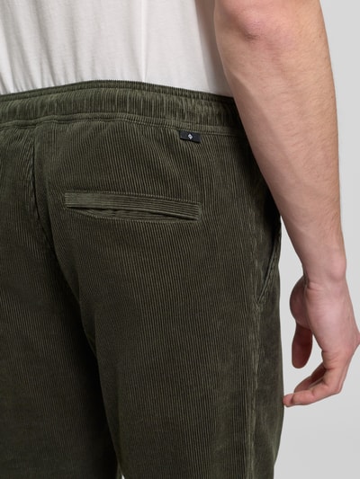 Männermodel trägt Cordhose mit elastischem Bund Modell 'JABARI' von Samsøe Samsøe in Olivgrün, Gesäßtasche, Nahaufnahme Rückansicht, Regular-Fit, Reine Baumwolle, Bundweite 42 cm, Innenbeinlänge 74 cm.