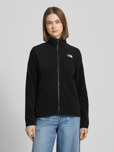 Frauenmodel trägt Fleecejacke mit Label-Stitching Modell 'GLACIER' von The North Face in Schwarz, Slim Fit, Stehkragen, Reißverschlusstaschen, Ganzkörperansicht von vorne, Kontext: Damen Fleecejacke, Rückenlänge 62 cm, Schulterbreite 39 cm, Brustweite 47 cm, Ärmellänge 62 cm, Größe S.