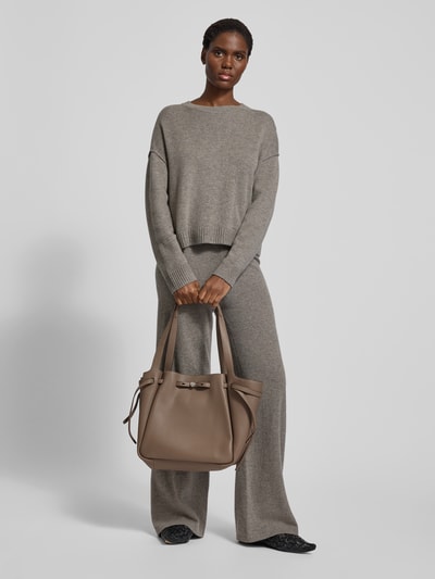Frauenmodel trägt Tote Bag mit Tragehenkel von Tory Burch in Beige mit Label-Detail, offenem Hauptfach und Innenfach mit Reißverschluss, Ganzkörperansicht von vorne.