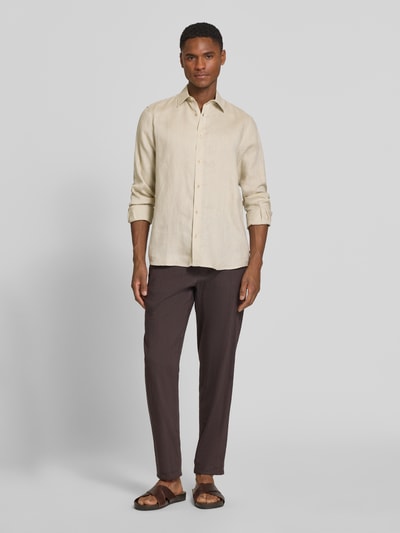 Męski model nosi Regular Fit Freizeithemd aus reinem Leinen von s.Oliver RED LABEL, efekt: jednolity kolor, krój regular fit, kołnierzyk typu kent, jednorzędowa listwa guzikowa, naszywka z logo, długi rękaw z mankietem, materiał: czysty len, kolor jasnobeżowy, gładka faktura, pełny widok z przodu.