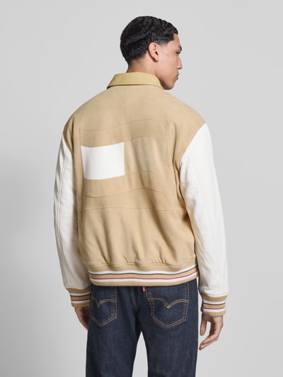 Männermodel trägt Relaxed Fit College-Jacke aus echtem Leder von Tommy Jeans in Beige und Weiß, Veloursleder-Optik, Ganzkörperansicht Rückansicht.