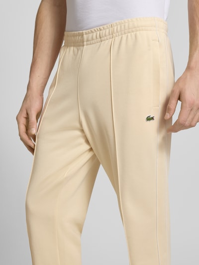 Männermodel trägt Regular Fit Sweatpants mit Baumwoll-Anteil von Lacoste in Beige mit Galonstreifen und Logo, Nahaufnahme Oberkörper.