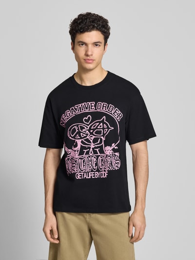 Männermodel trägt Herren T-Shirt POSITIVE CHAOS von Edwin, schwarze Baumwolle, Relaxed-Fit, Motiv-Print, Rundhalsausschnitt, Ganzkörperansicht von vorne. Rückenlänge bei Größe M: 70 cm.