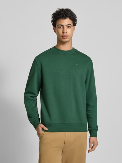 Männermodel trägt Regular Fit Sweatshirt aus Baumwoll-Mix von Tommy Jeans in Optik: Unifarben mit Logo-Stitching, Ganzkörperansicht von vorne.
