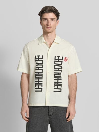 Männermodel trägt Regular Fit Freizeithemd mit Label-Print Modell 'Banks' von WOODBIRD in Hellbeige, Kentkragen, Ganzkörperansicht von vorne. Rückenlänge bei Größe M: 76 cm, Schulterbreite: 52 cm, Ärmellänge: 28 cm.
