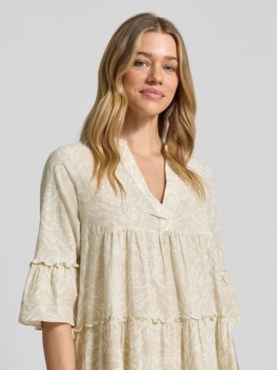 Vrouwenmodel draagt Ausgestelltes Blusenkleid aus reiner Baumwolle Modell 'DICTHE' van Vero Moda in beige met allover-patroon, Henley-hals, ruches, trompetmouwen, mini lengte; pure katoen, rechte pasvorm, detailopname bovenlijf.