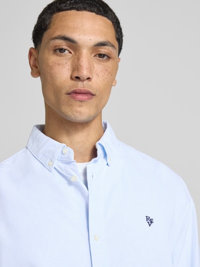 Męski model nosi koszulę casualową z czystej bawełny Freizeithemd aus reiner Baumwolle od REVIEW, wyhaftowane logo, Kołnierzyk typu button down, prosty krój, długi rękaw, mankiety zapinane na 1 guzik, jasnoniebieska, gładka faktura, zbliżenie na górną część tułowia.