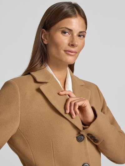 Frauenmodel trägt Mantel aus Woll-Mix mit Reverskragen und Pattentaschen von FUCHS SCHMITT in Beige, glatte Textur, Nahaufnahme Oberkörper. Straight Fit, Knopfverschluss, Kaschmir-Anteil, dezente Knöpfe und feine Struktur, KI-modifiziertes Bild.