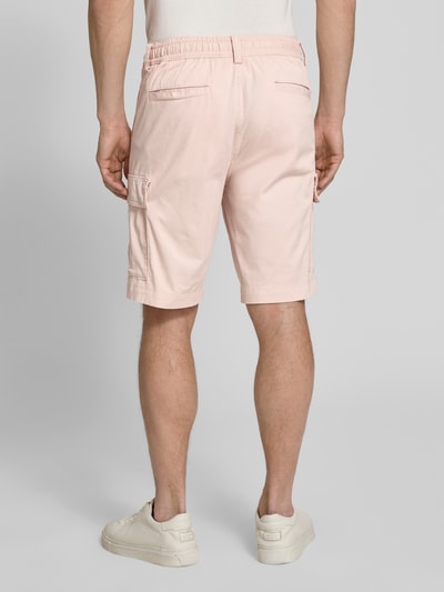 Männermodel trägt Relaxed Fit Cargoshorts aus Baumwoll-Mix Modell 'SISLA' von BOSS Orange in zartem Rosa, Details wie Cargotaschen, unifarbene Optik, Label Patch, Knopfverschluss und Gürtelschlaufen, Ganzkörperansicht Rückansicht.